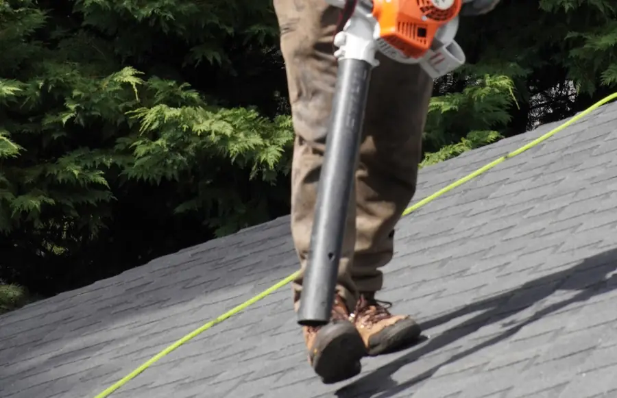 Titan Roofing crew member clearing debris from a shingle roof with a leaf blower