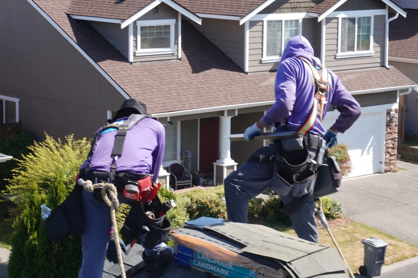 Two Titan Roofing roofers in harnesses and safety lines working on a shingle roof
