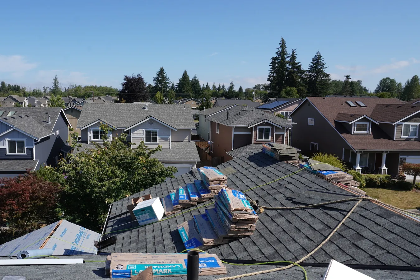 Roof replacement in progress with CertainTeed Landmark shingle bundles and safety lines on the roof